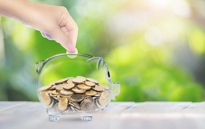 In ein transparentes mit Münzen gefülltes Sparschwein wird eine Münze geworfen